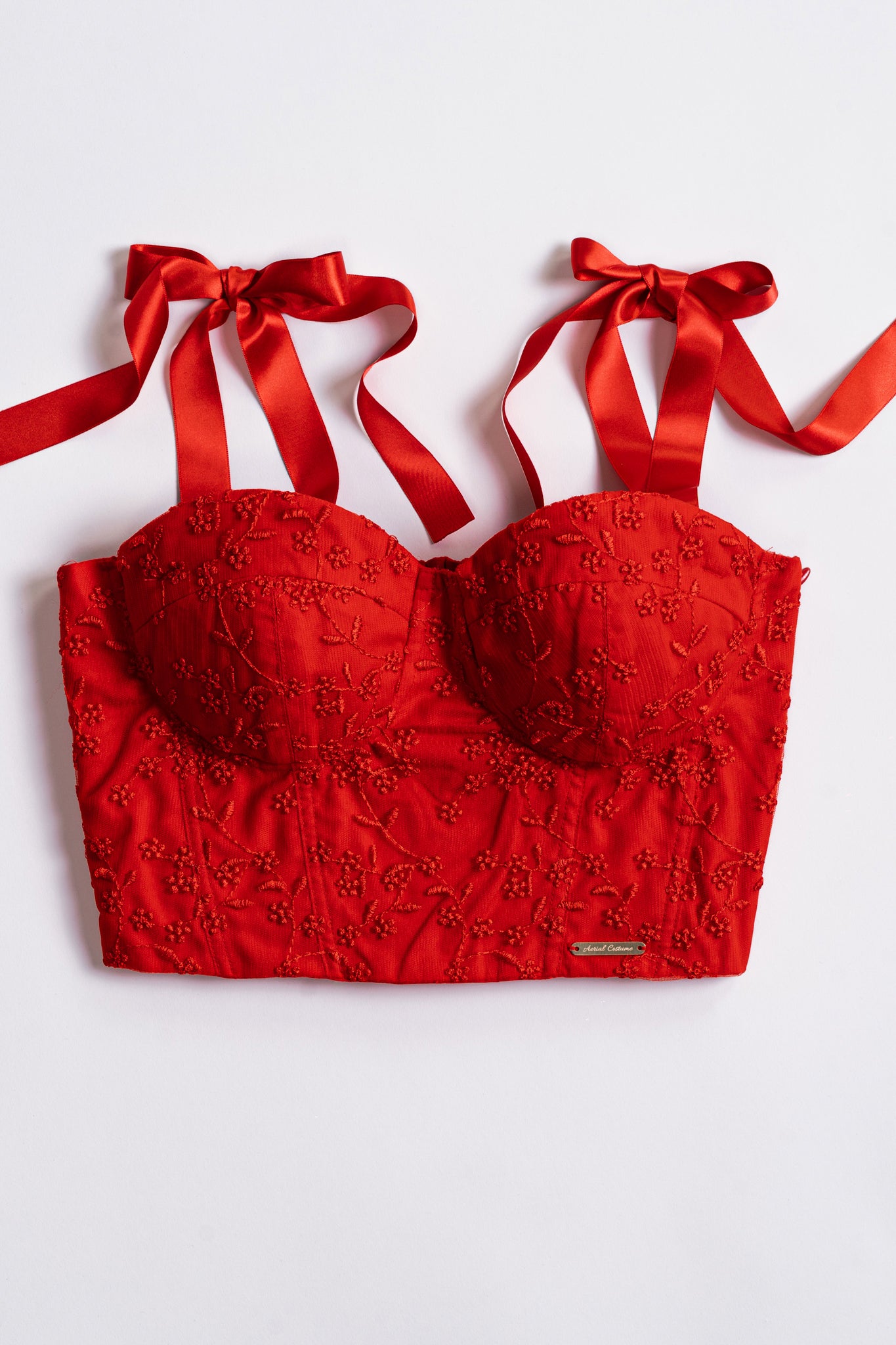 Bustino rosso ricamato con motivi floreali e spalline a fiocco su sfondo bianco